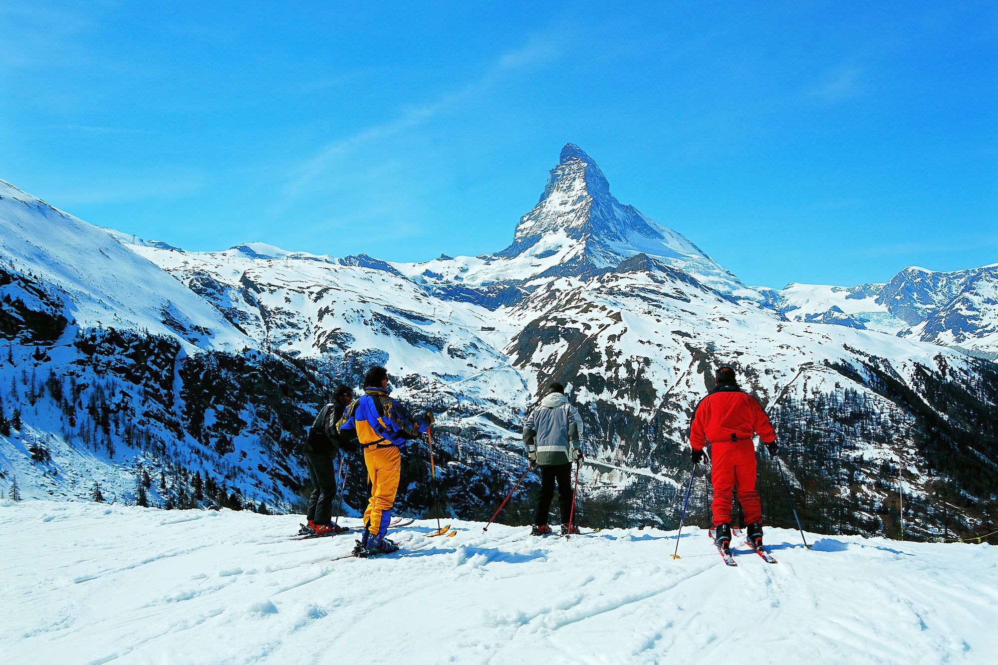 Four skiers on a snowy ridge above Zermatt looking across at the Matterhorn
