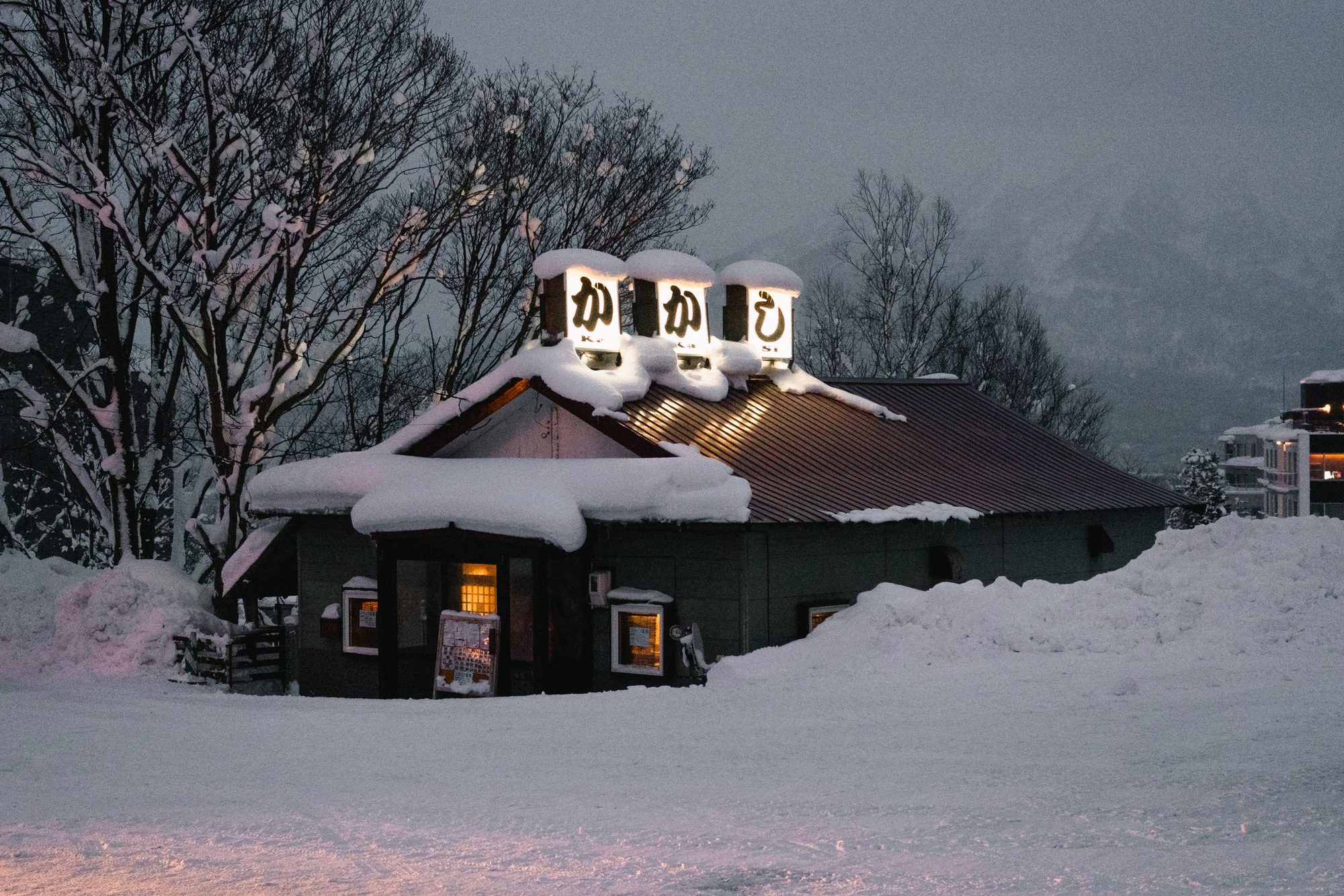 A snow-covered izakaya lit by paper lanterns on a winter evening in Niseko
