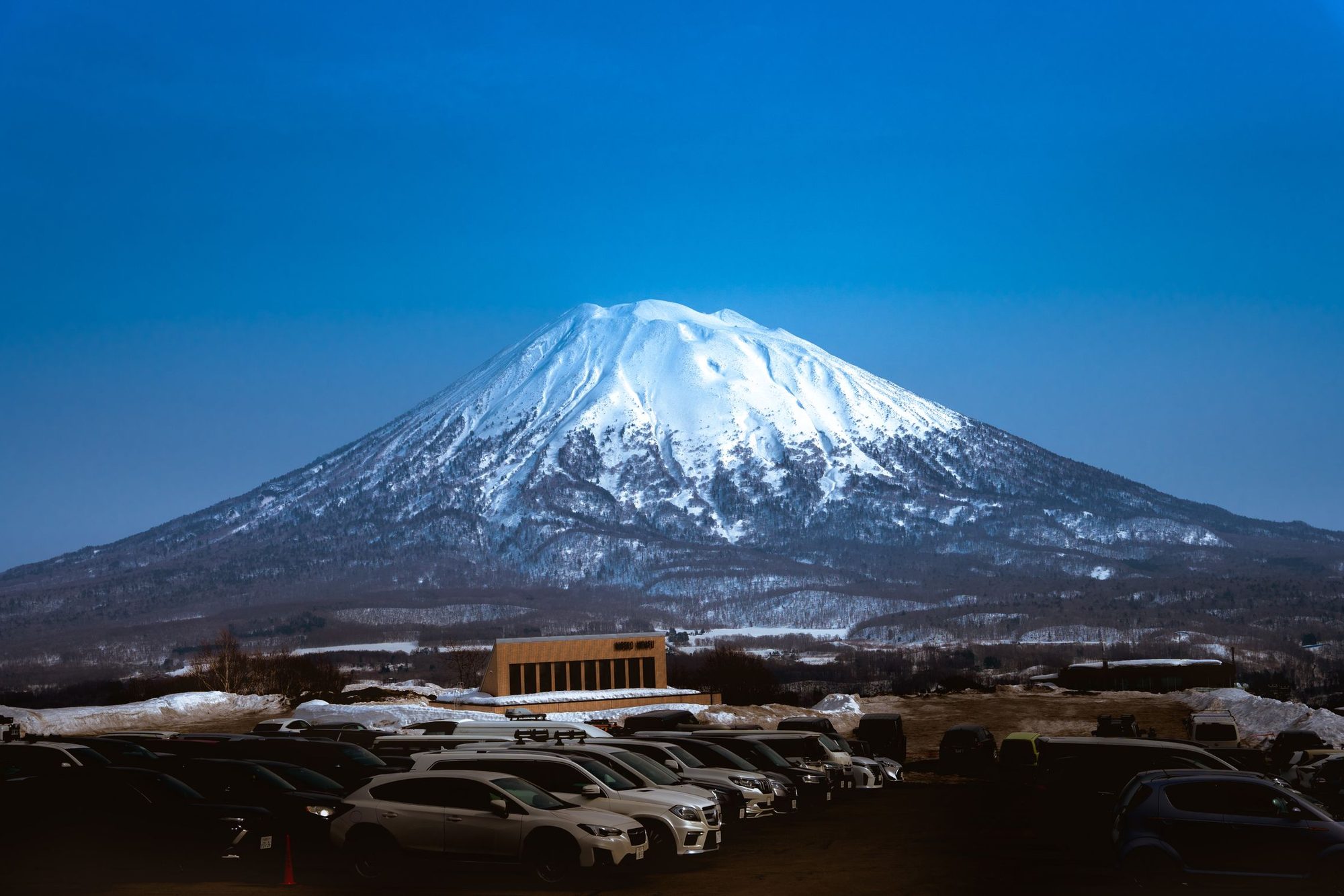 Mount Yōtei under snow at dusk, seen across a car park in Niseko