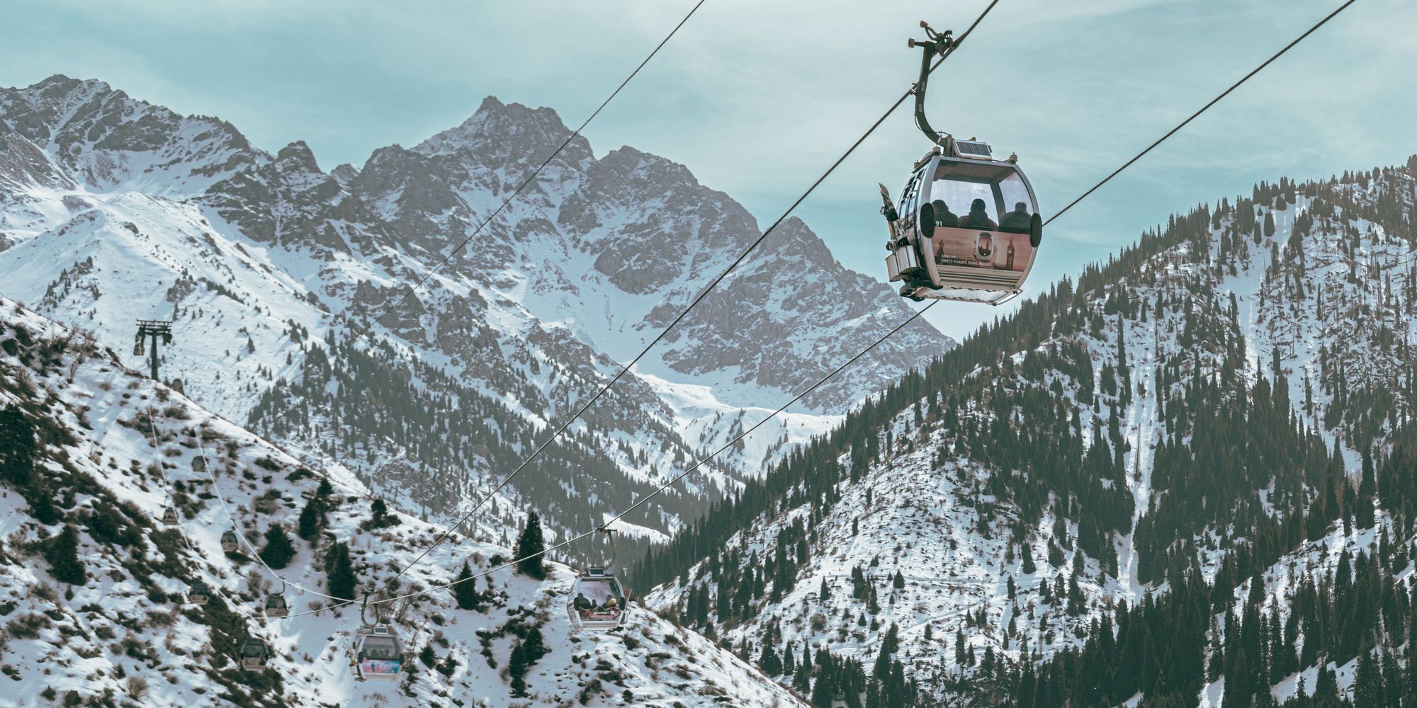 A gondola cabin crossing a snowy, forested valley on the way up from Medeu