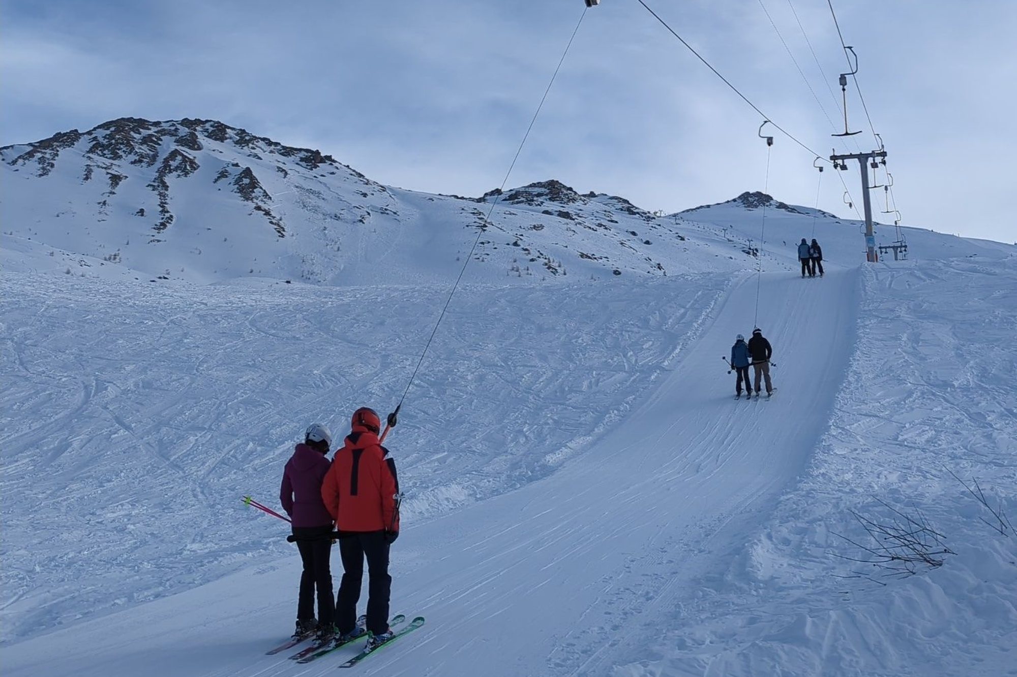 Skiers riding a drag lift up a snowy slope at Nendaz