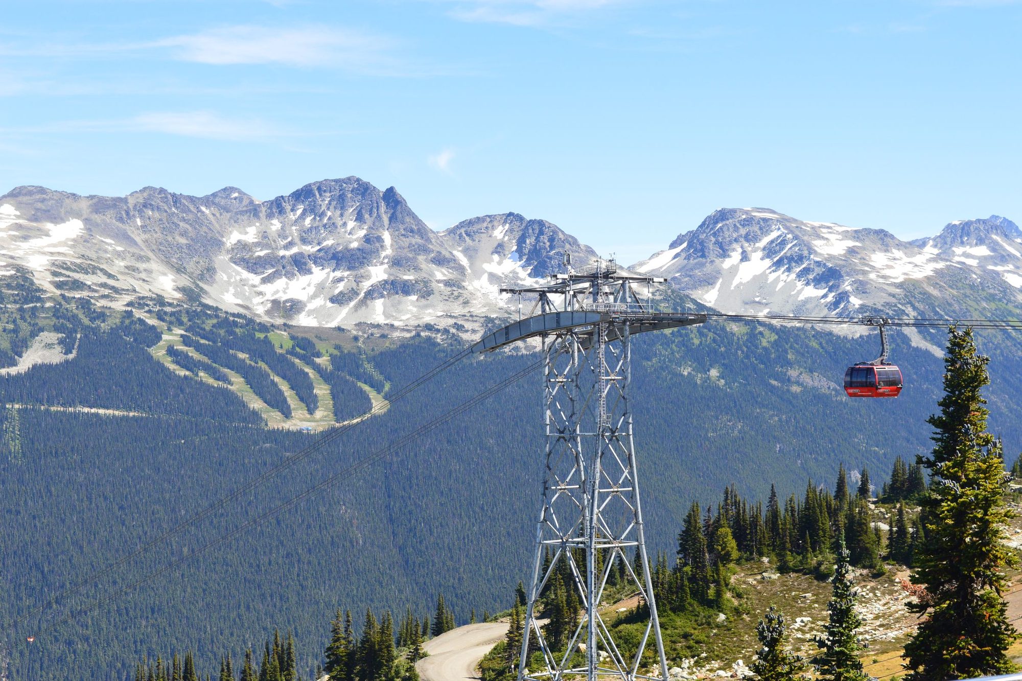 A red Peak 2 Peak gondola cabin crossing between towers, with the runs of Blackcomb Mountain behind