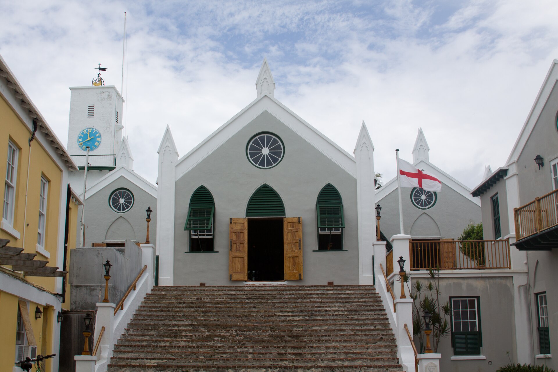 The white rendered front of St Peter's Church with a stepped approach, arched doors and windows, green shutters and a clock tower at the left