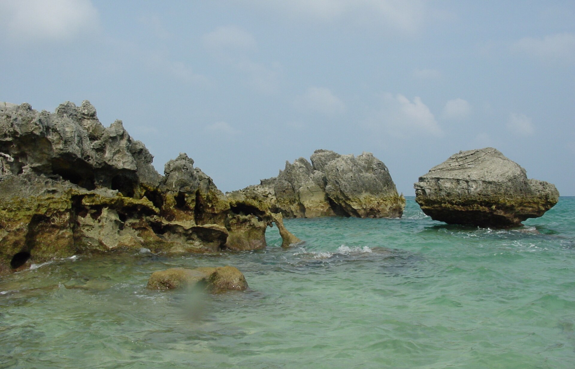 Weathered limestone stacks standing in shallow clear turquoise water off a beach, under a bright sky