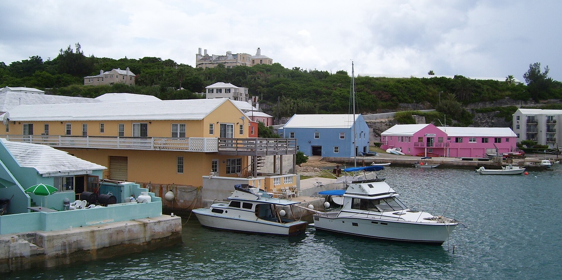 St George's Harbour with yellow and pink waterfront buildings, a quay and moored motor yachts under a grey sky