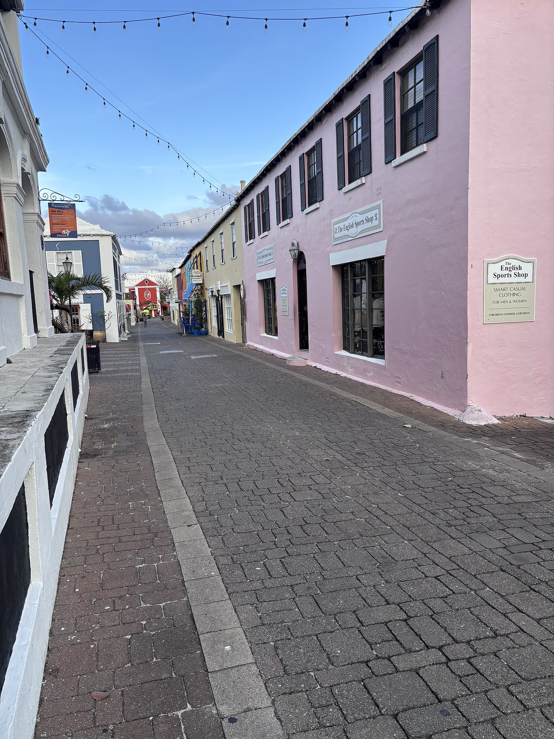 A narrow stone paved lane in St George's between pink and white two storey buildings with dark shutters, bunting strung overhead