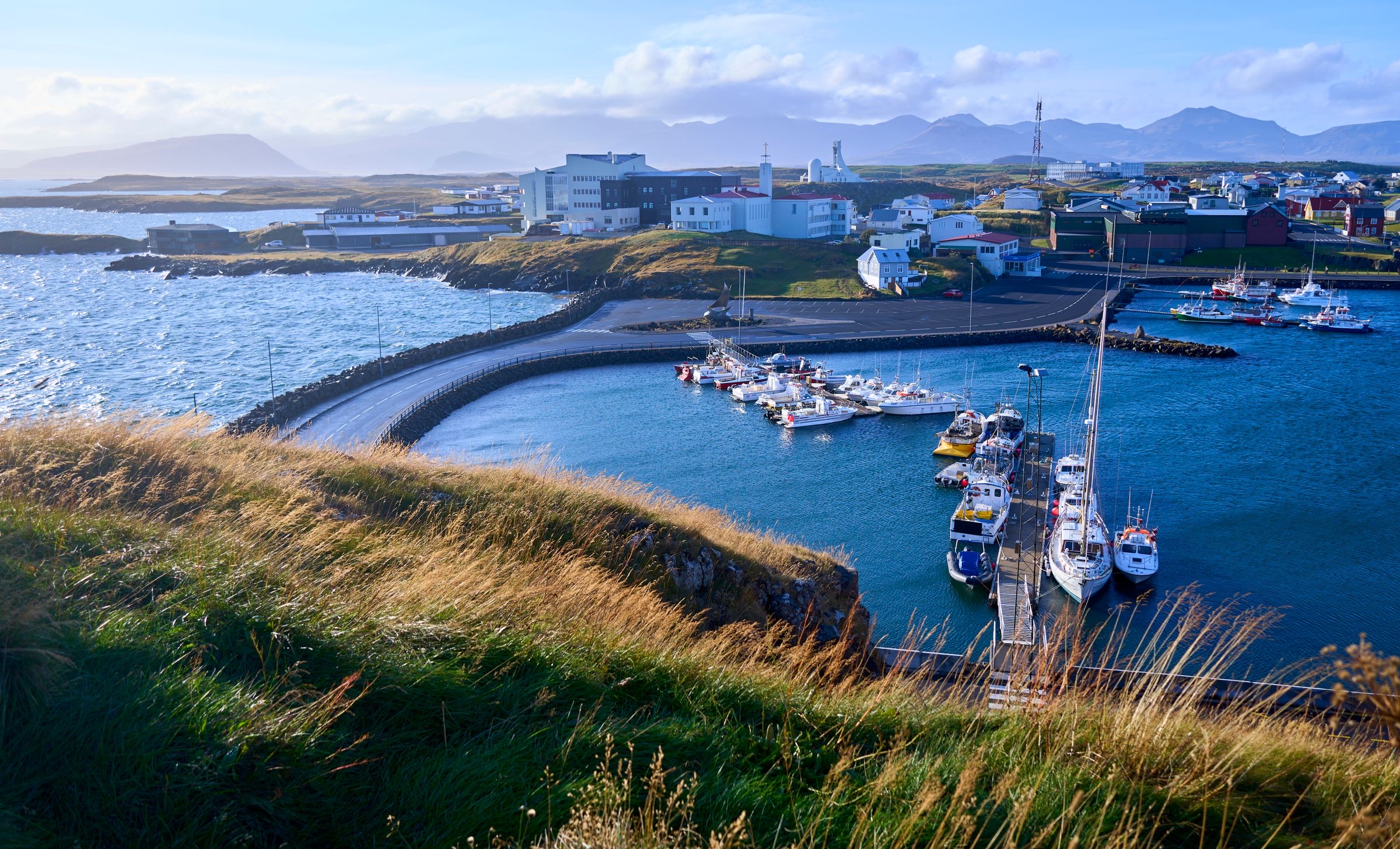 Stykkishólmur's marina and causeway seen from the slope of Súgandisey, with the white church tower on the skyline and mountains across the bay