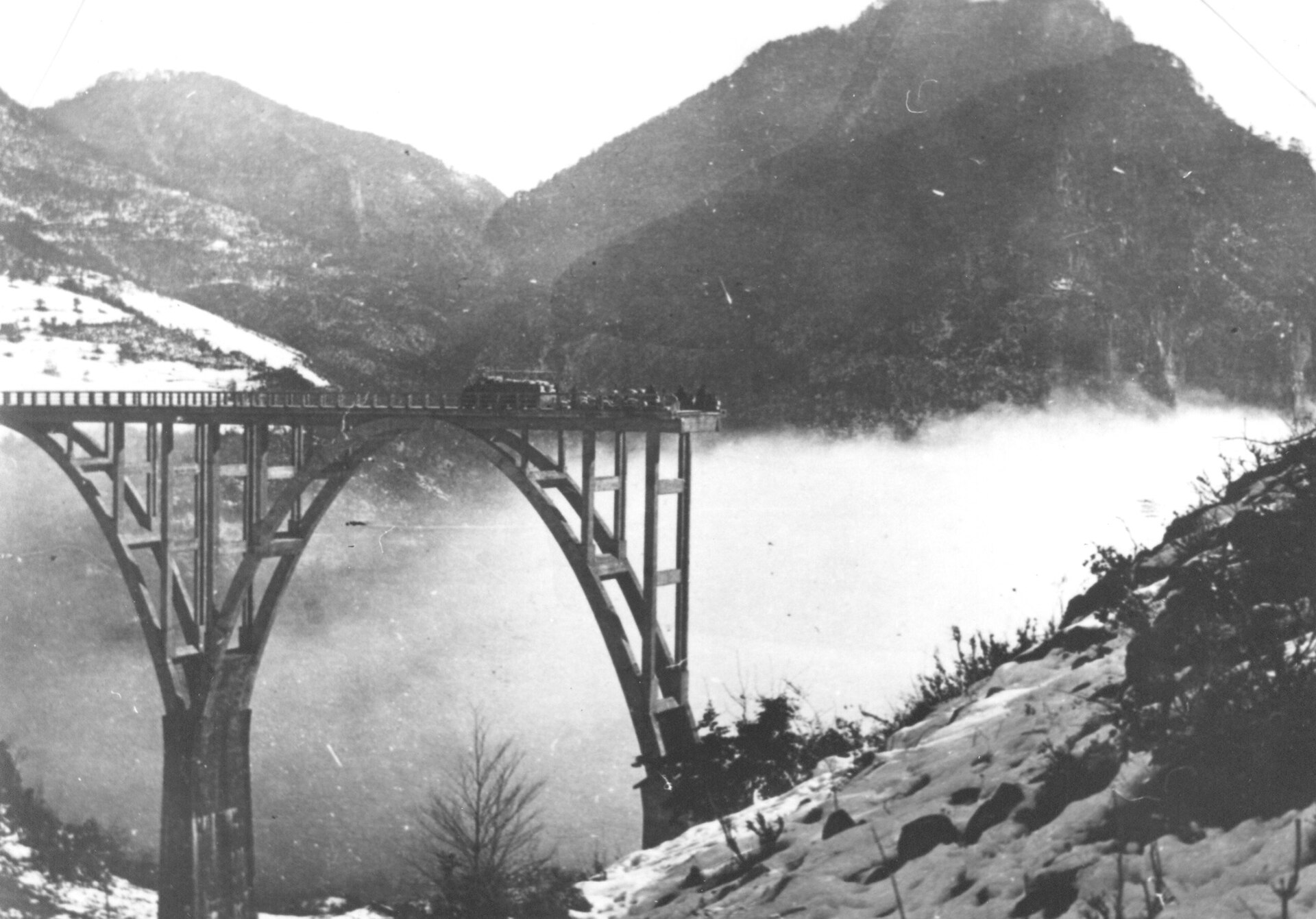 A black and white photograph of the Tara bridge in snow on 6 December 1943, with figures standing on the deck