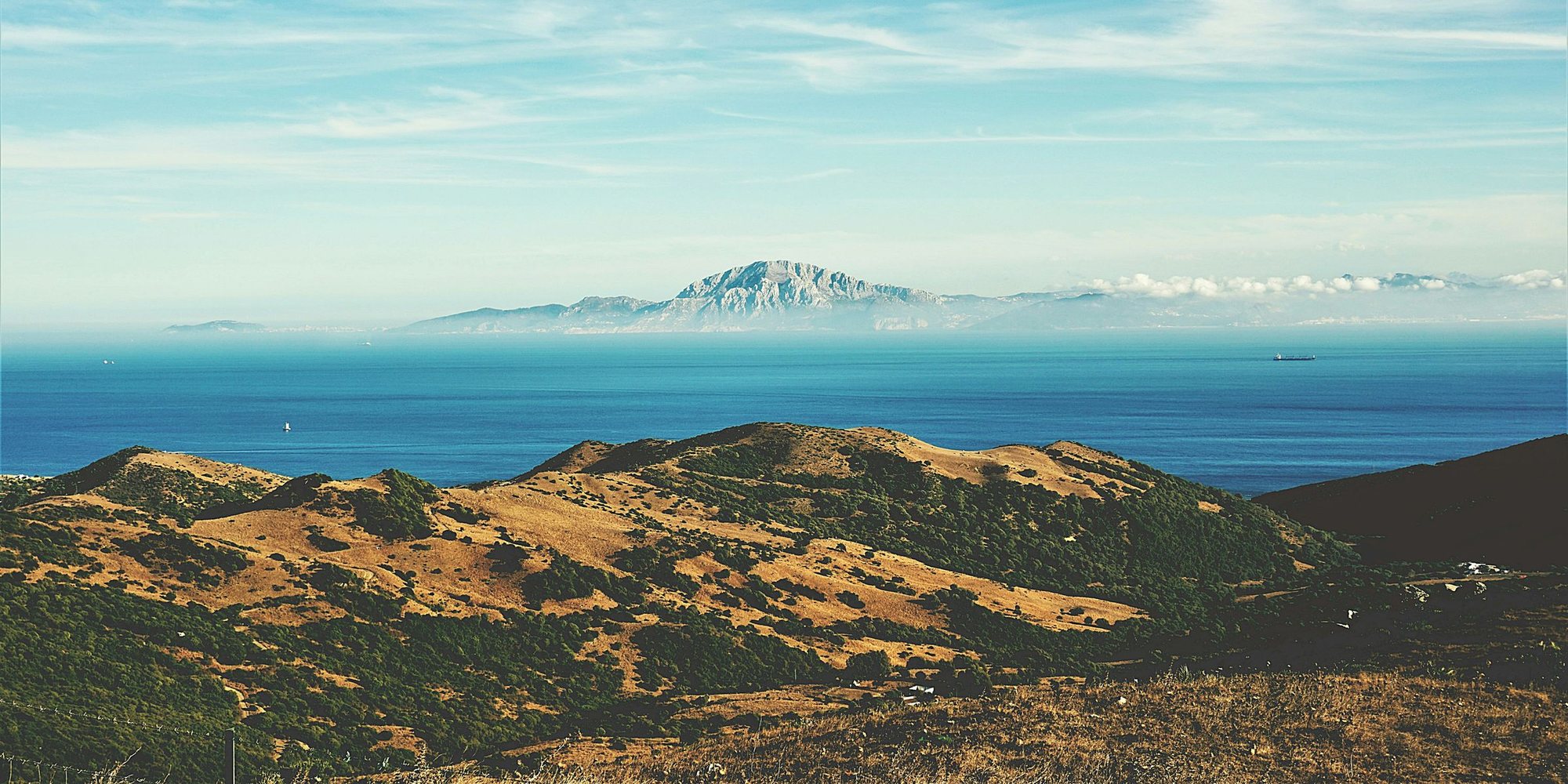 The Strait of Gibraltar from the hills above Tarifa, dry green ridges in front and the mountains of Morocco across blue water