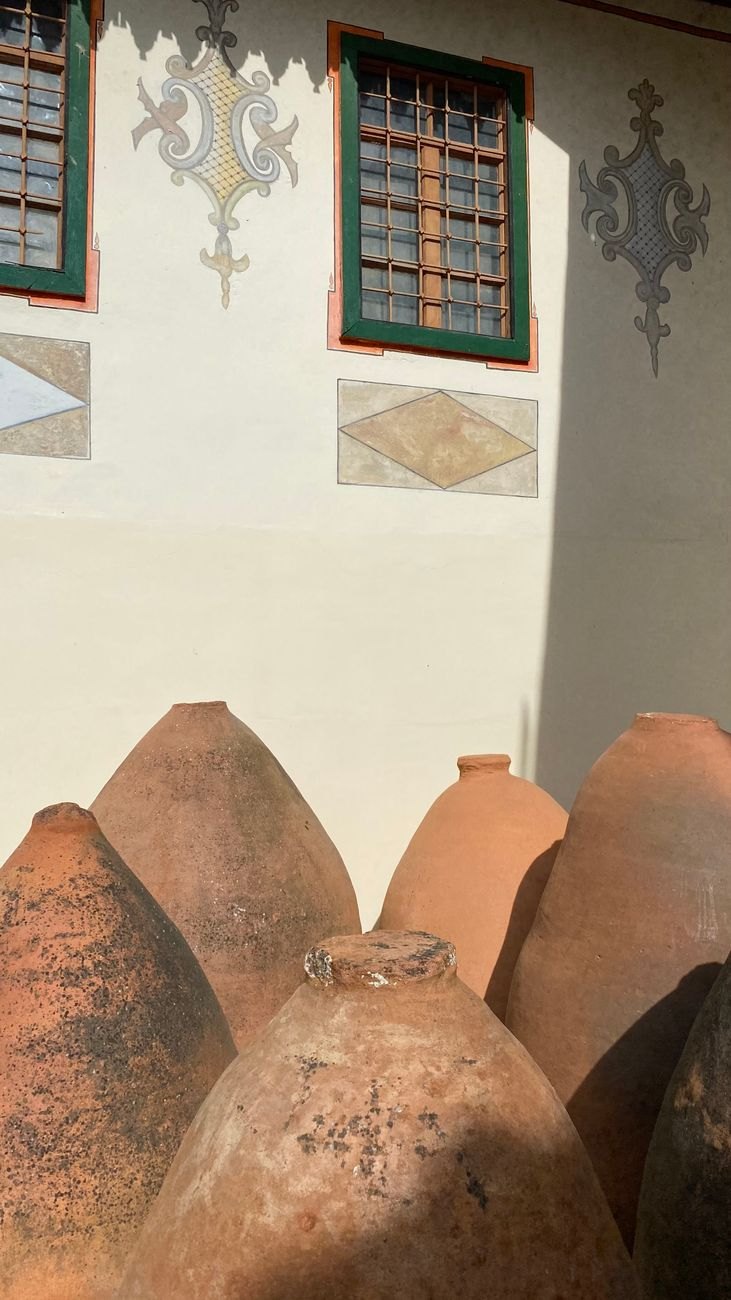 Large egg-shaped terracotta qvevri, the clay vessels Georgian wine ferments in, below a painted old-town wall