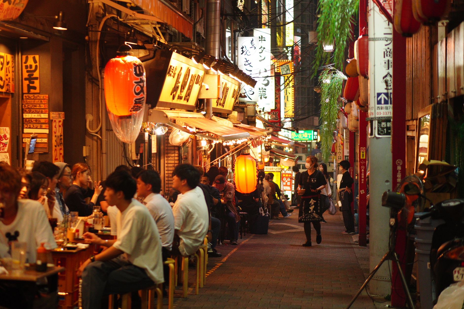 A narrow alley of tiny bars lit by lanterns and neon at night in Tokyo
