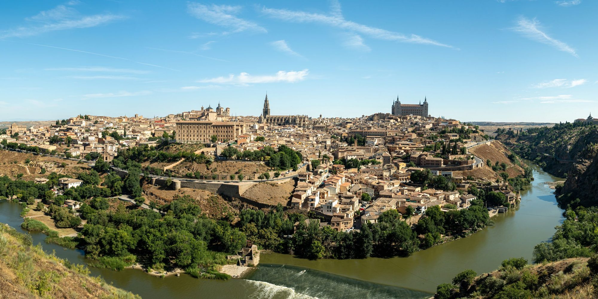 Toledo on its hill above a bend of the Tagus, the cathedral spire on the left and the square Alcázar on the right