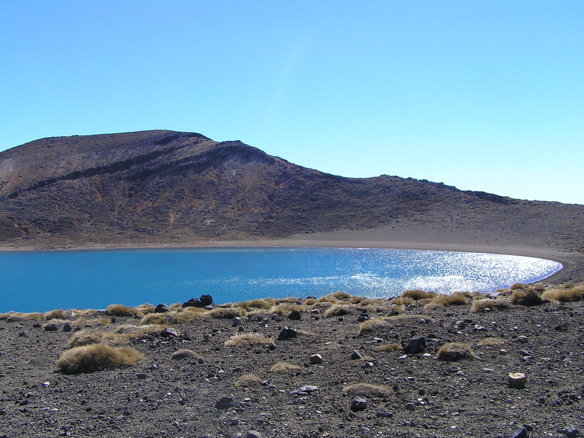 A deep blue alpine lake below a bare volcanic ridge in hard clear light