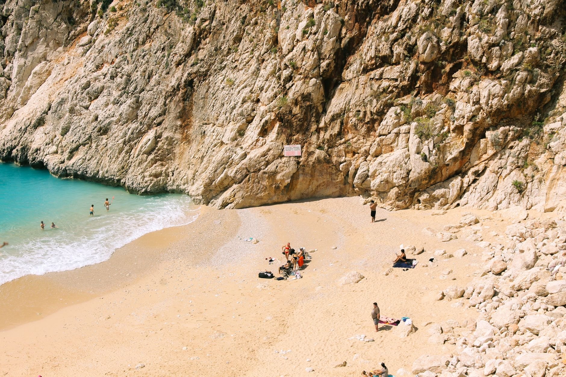 A crescent of pale sand at the foot of a limestone gorge, with clear turquoise water and a few swimmers, at Kaputas between Kas and Kalkan