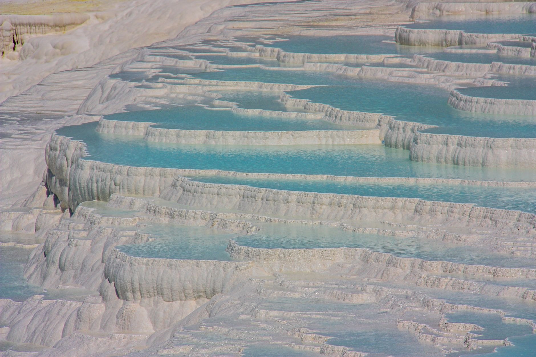 The white travertine terraces of Pamukkale stepping down the hillside, each shelf holding a shallow pool of pale turquoise water