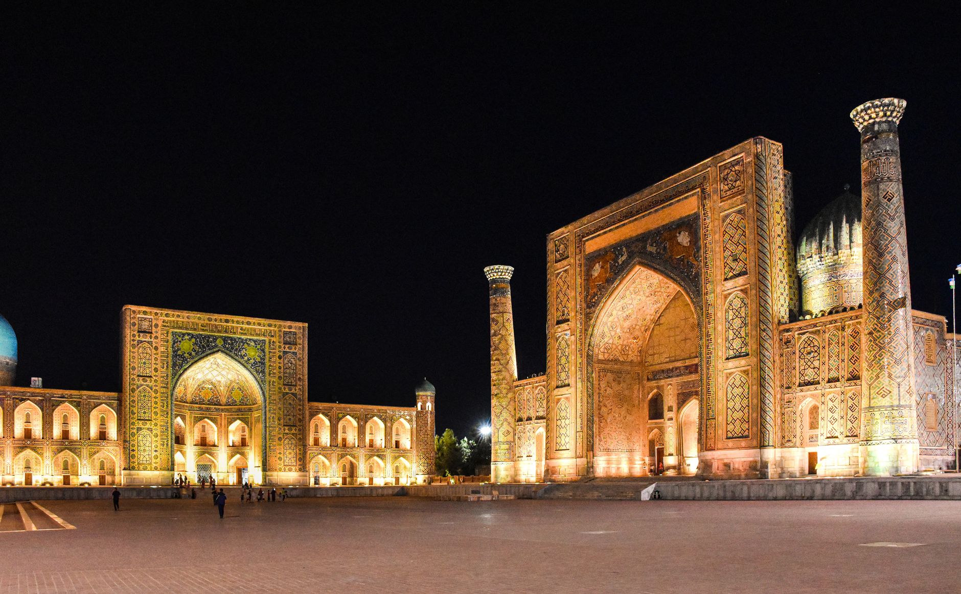 The Registan in Samarkand lit at dusk, its three tiled madrasas glowing against a blue sky