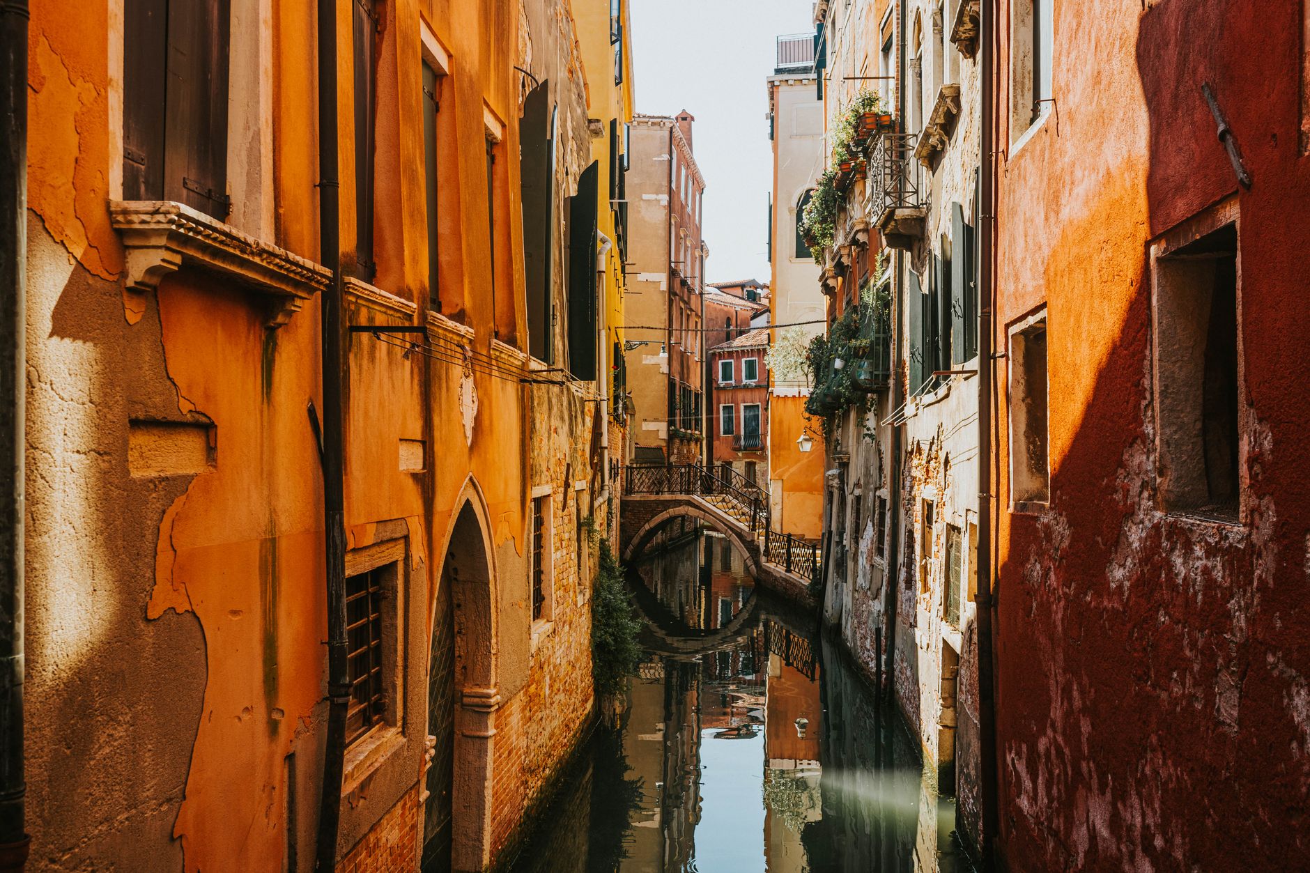 A quiet narrow Venetian canal between warm ochre and orange palazzo walls, a small bridge crossing it