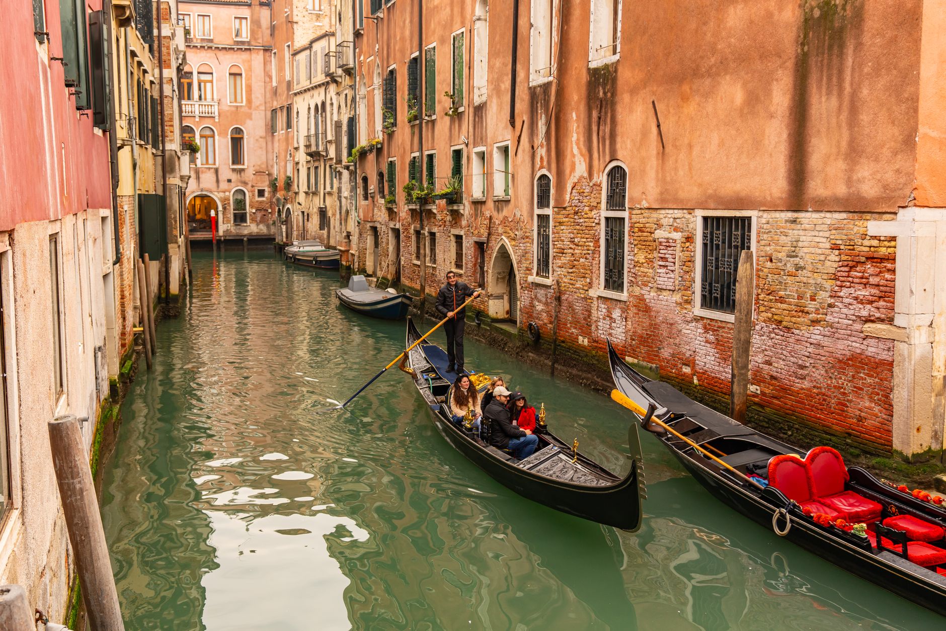 A gondola gliding through a quiet green side canal in Venice between old brick buildings