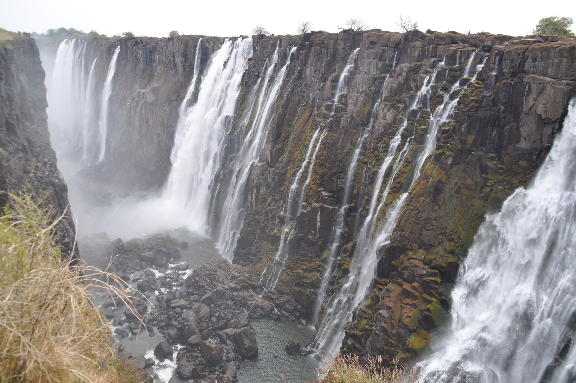 Many separate falls running down a long basalt face at Victoria Falls, with bare rock showing between them