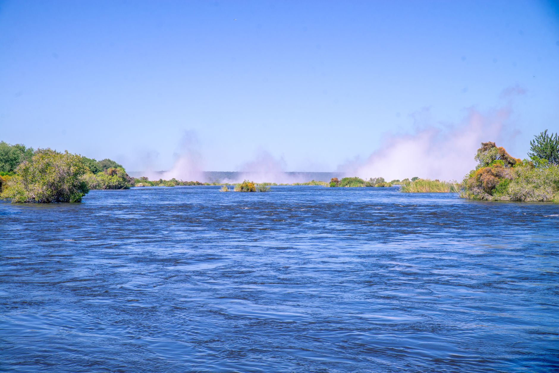 The wide Zambezi upstream of the falls with mist rising in the distance