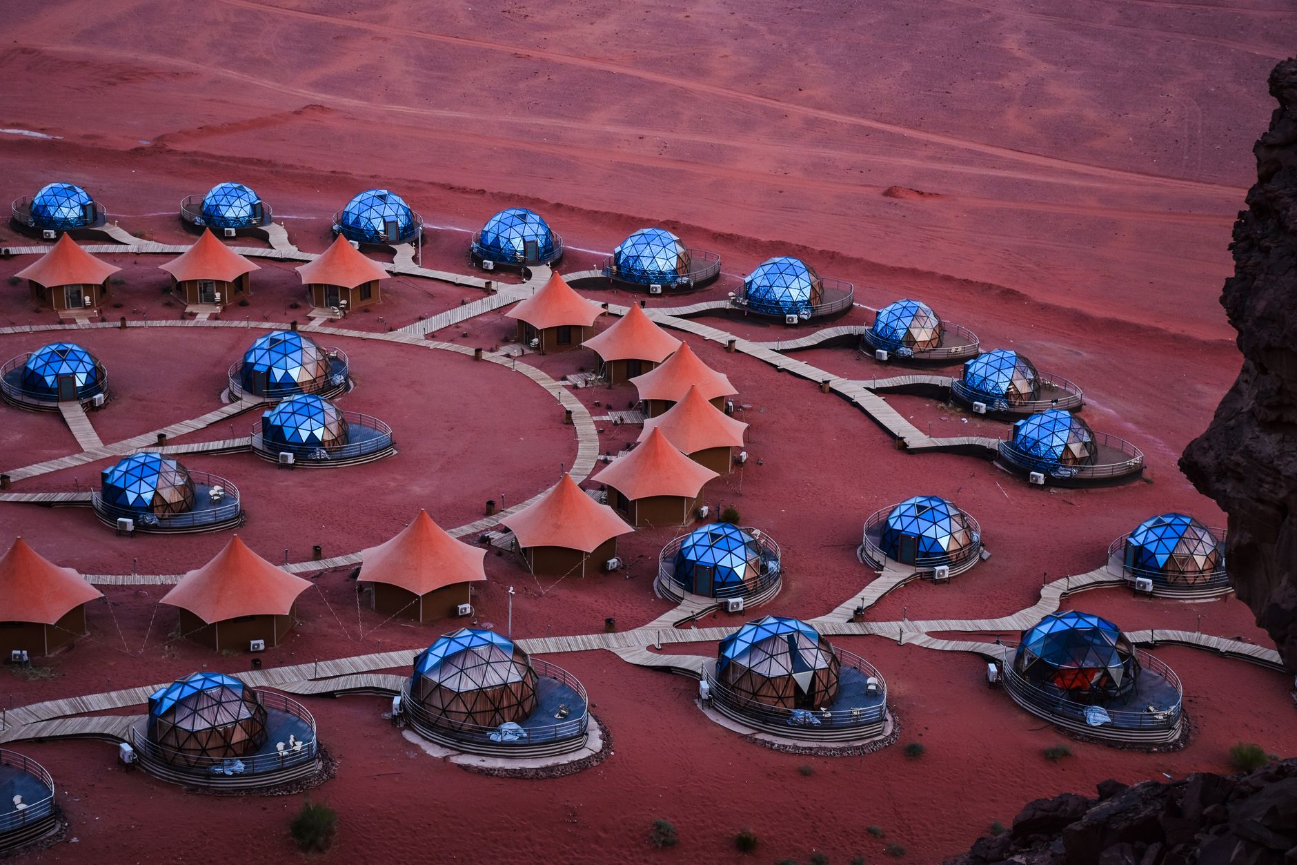 Aerial view of a Wadi Rum camp of blue geodesic domes and peaked tents linked by boardwalks on red sand