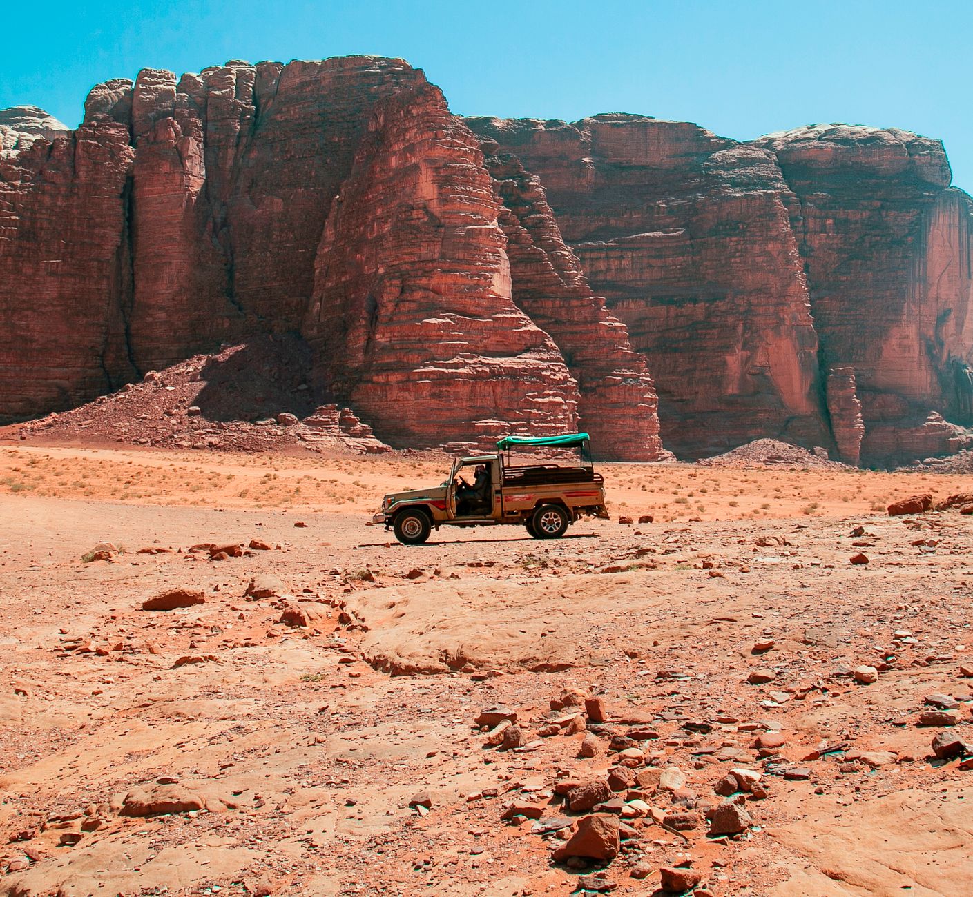 A canopied Toyota pickup with bench seats in the bed, on the desert floor below a sandstone massif in Wadi Rum