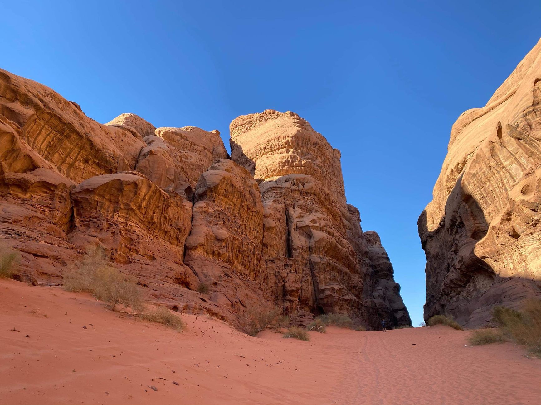 A single walker on red sand in the gap between two sandstone massifs in Wadi Rum