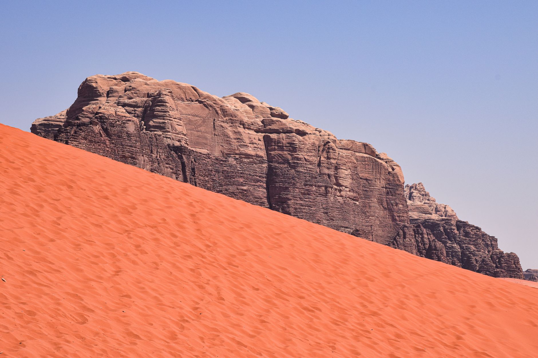 A steep dune of deep red sand meeting a sandstone cliff in Wadi Rum