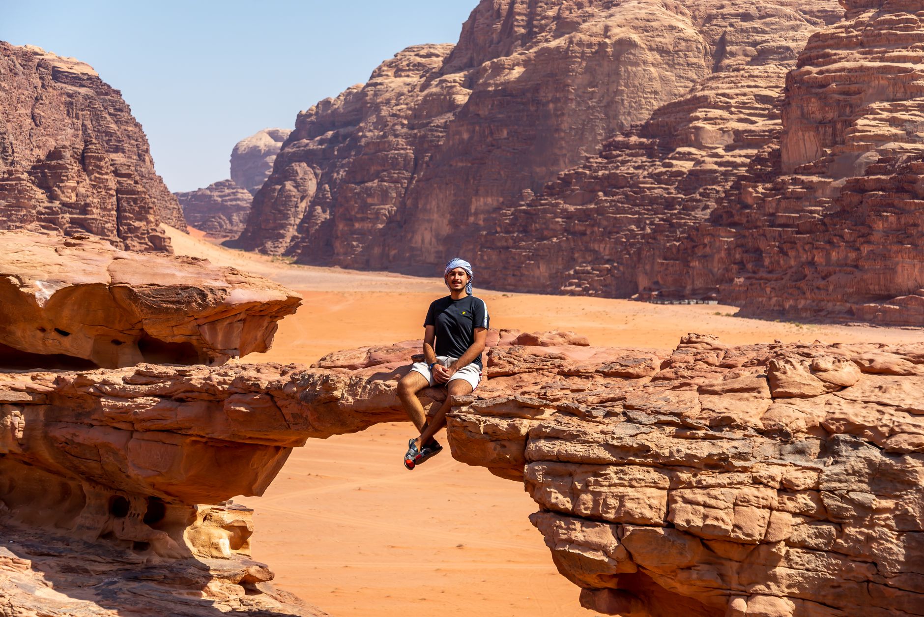 A person sitting on top of a natural sandstone rock bridge in Wadi Rum