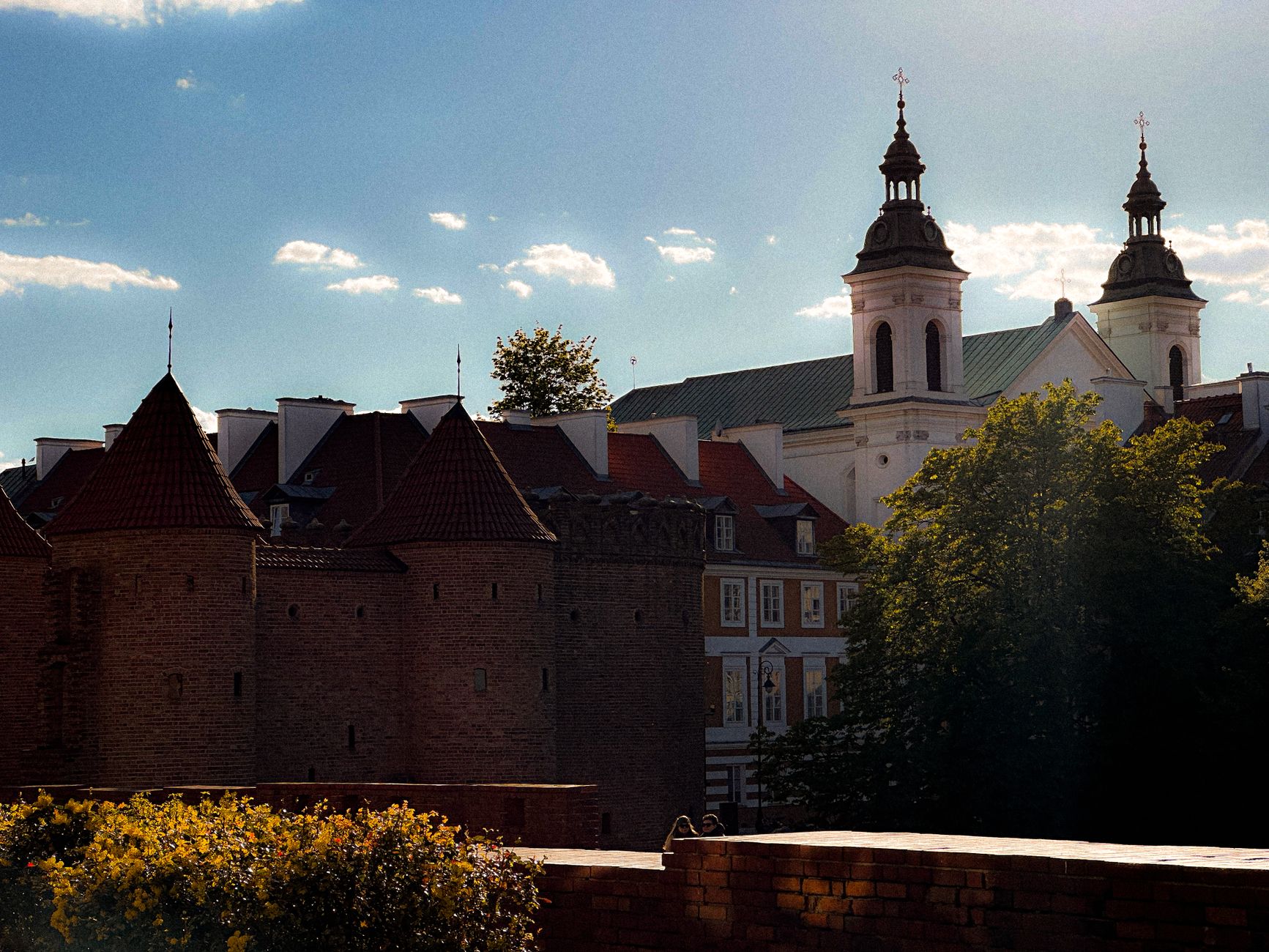 The red-brick Barbican in Warsaw with a church tower behind it under a blue sky