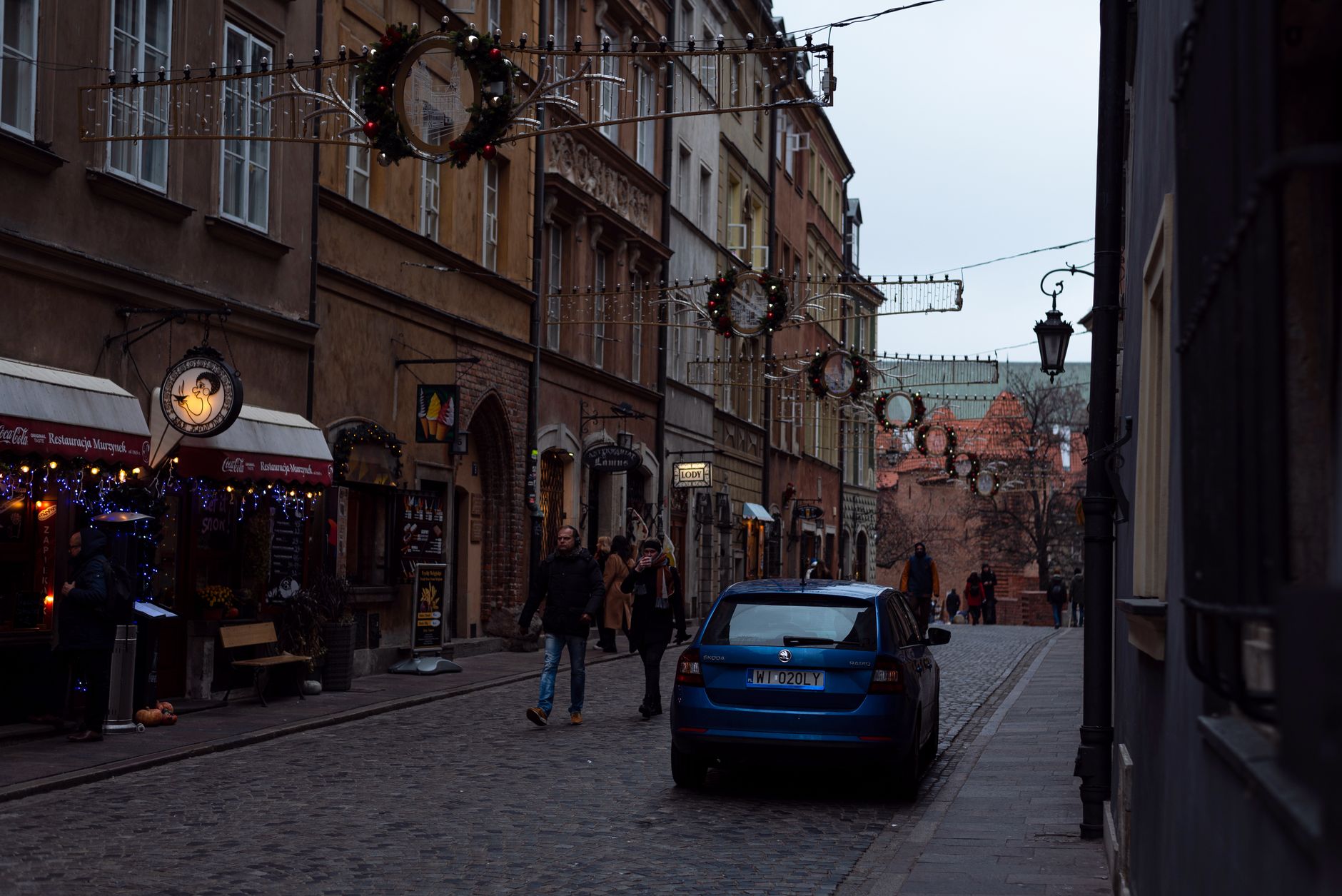 A cobbled street in Warsaw Old Town at dusk, hung with festive decorations