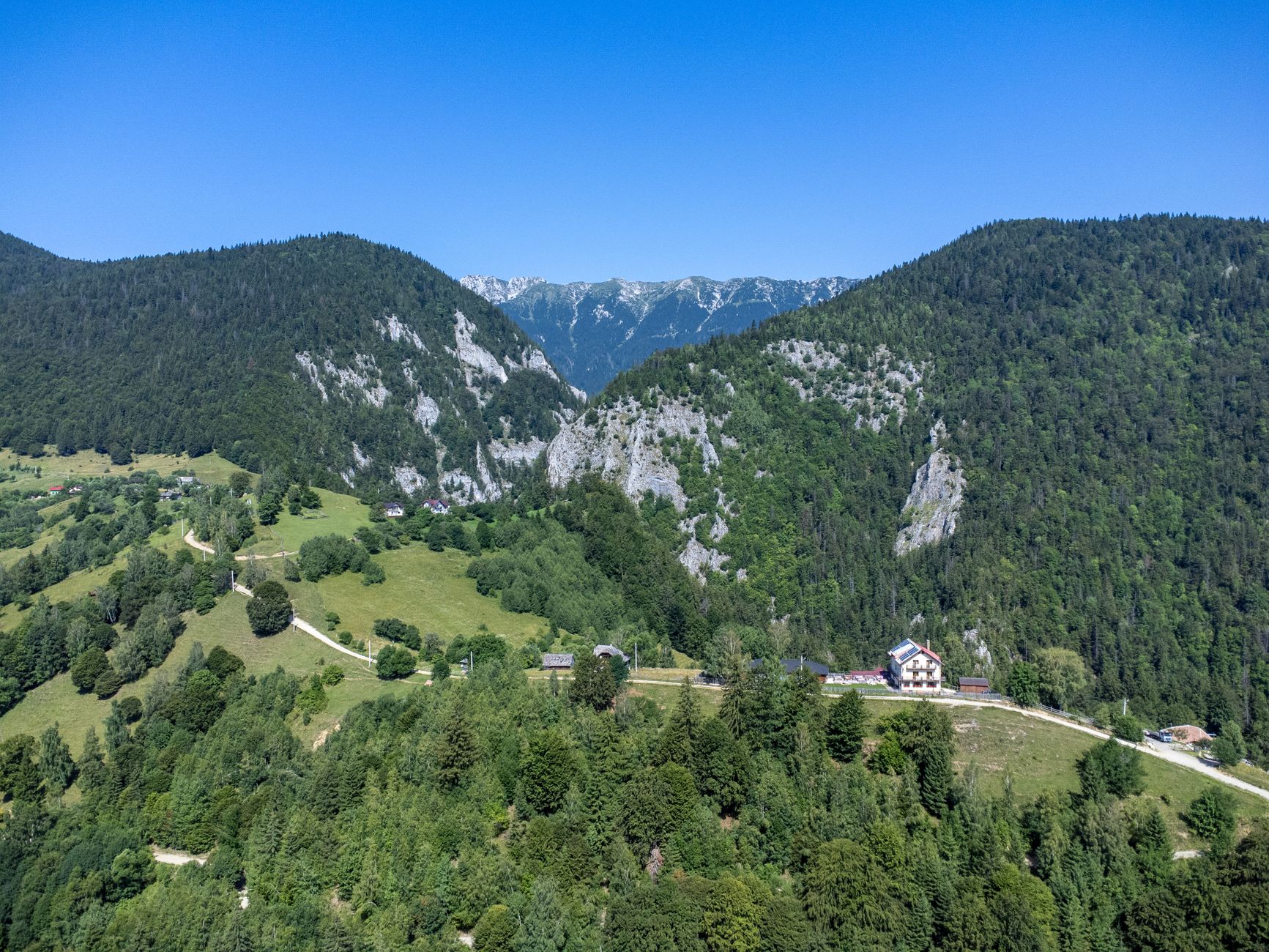 An aerial view of scattered houses and hay meadows at Măgura with the Piatra Craiului ridge behind